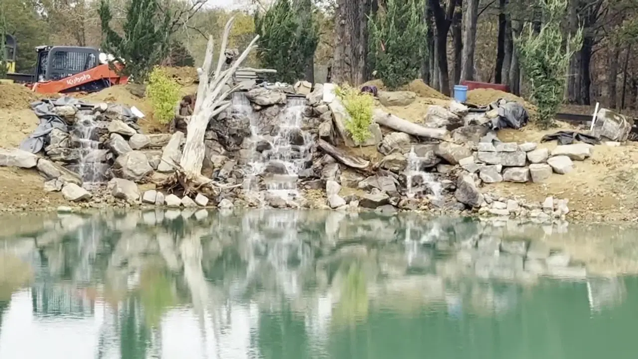 Boulder waterfall spilling into a lake pond, the machine still on site