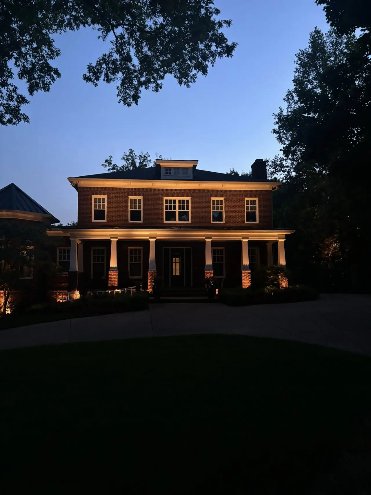 A brick house and its front trees lit at dusk