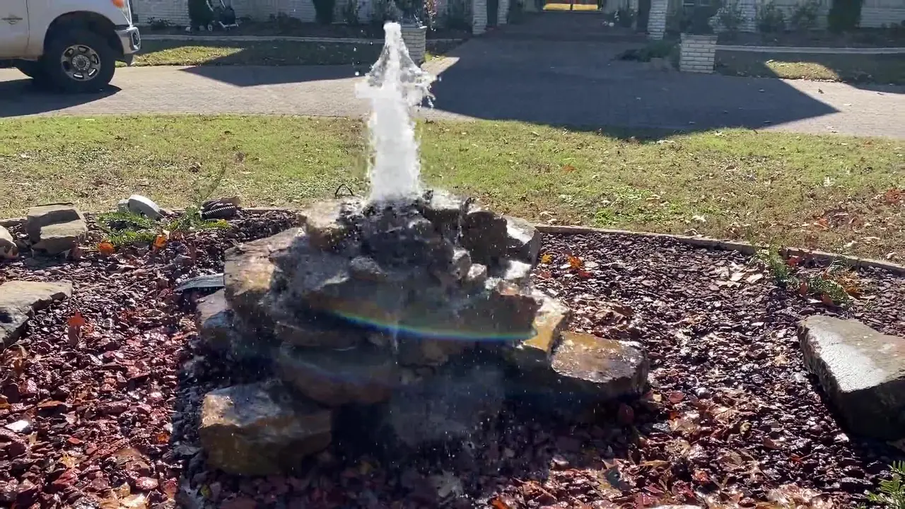 A bubbling rock fountain in a mulched bed by the driveway