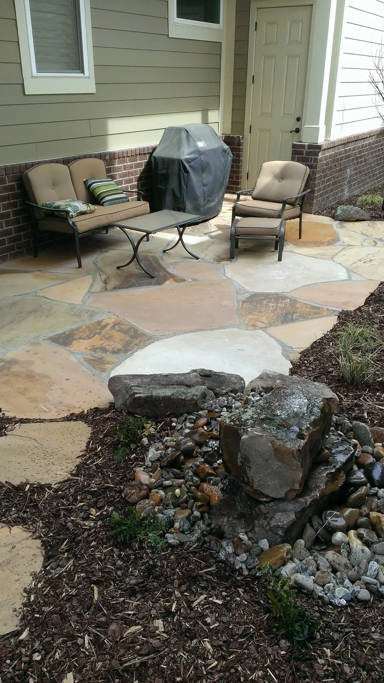A flagstone patio with chairs and a grill beside the house
