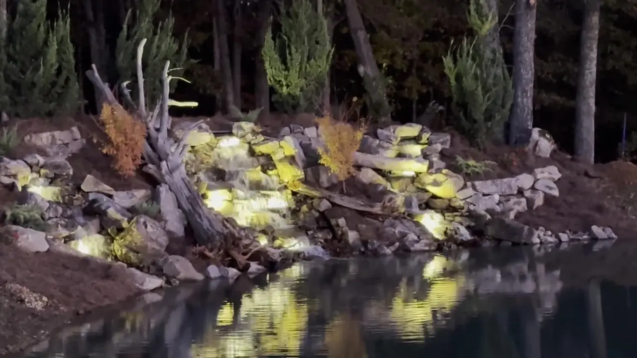 The same lakeside waterfall lit after dark