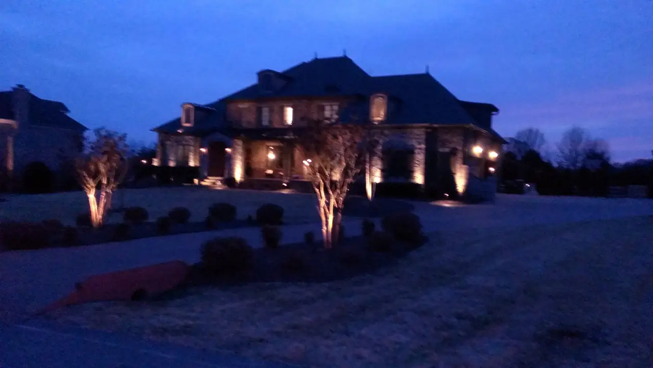A large stone house and its trees uplit at dusk
