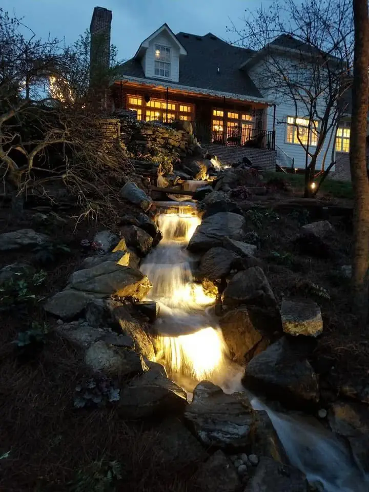 A lit stream running toward the house at dusk