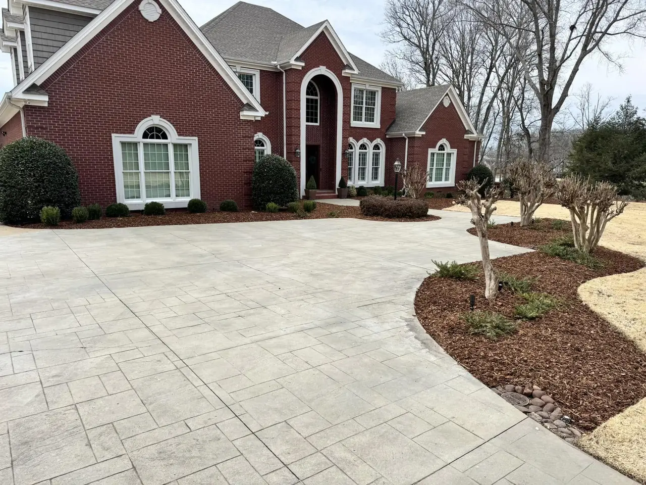 A stamped concrete drive and planted beds at a brick house