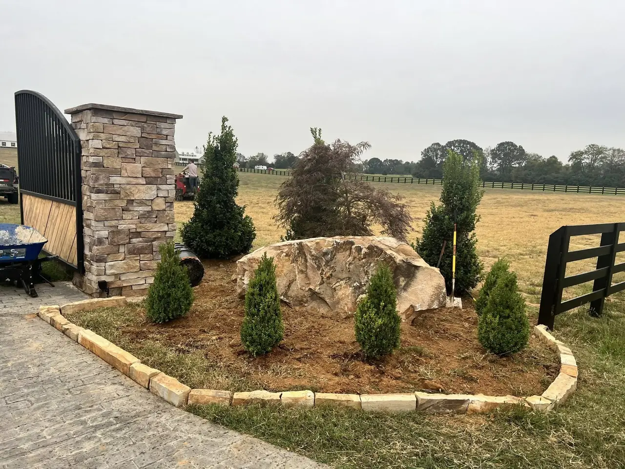 Stone entry pillars and a boulder bed with evergreens