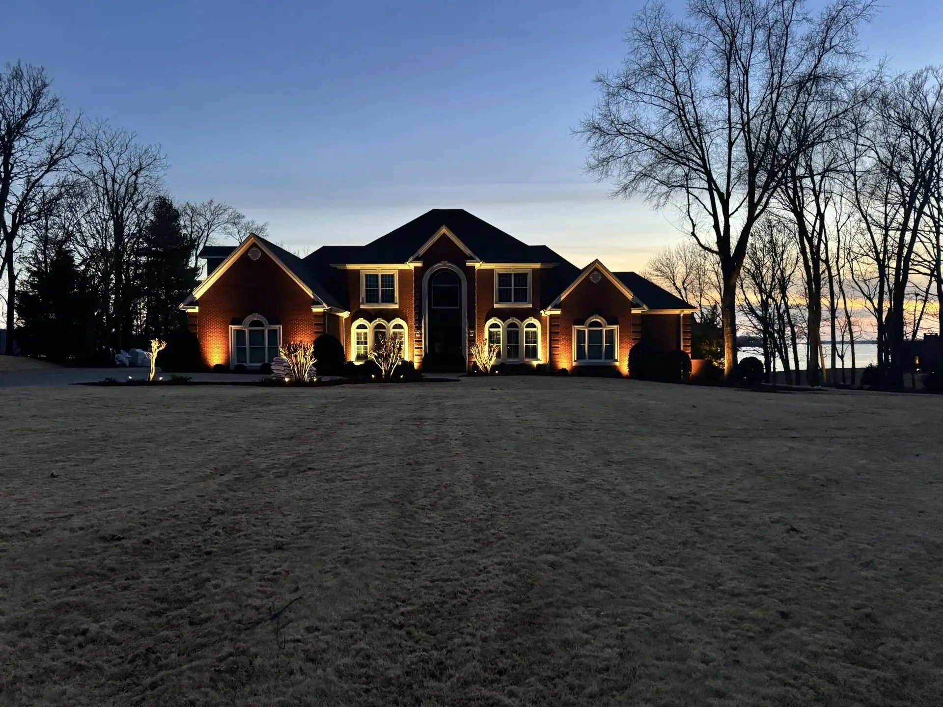 A brick house washed with uplighting at dusk, seen across the front lawn