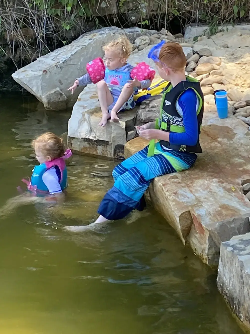 Children playing on the boulders of a natural swim pond