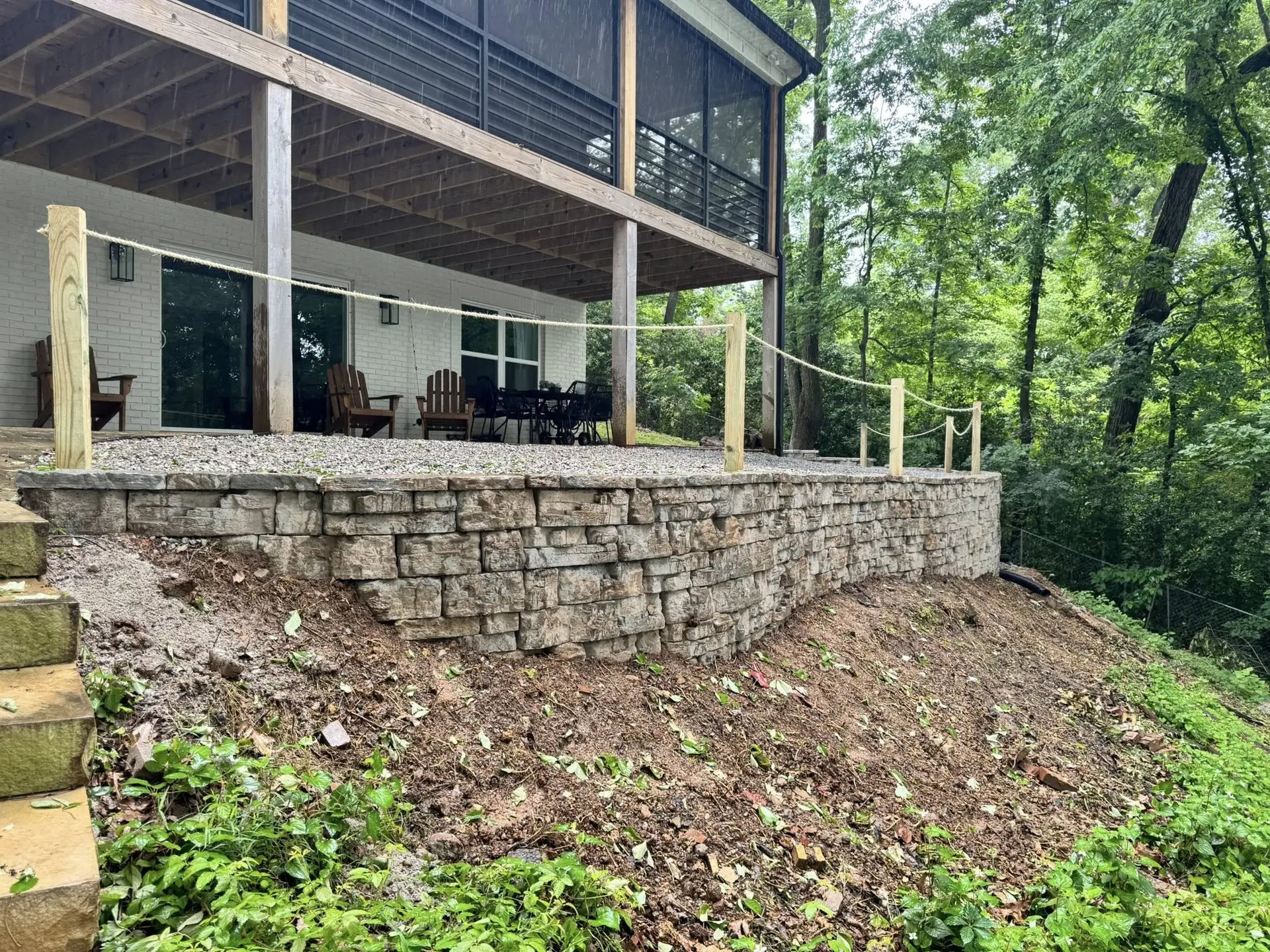 Dry-stacked stone retaining wall holding the slope under a screened deck