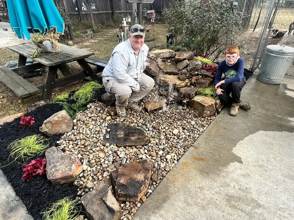 A finished rock garden with a man and a young helper crouched beside it
