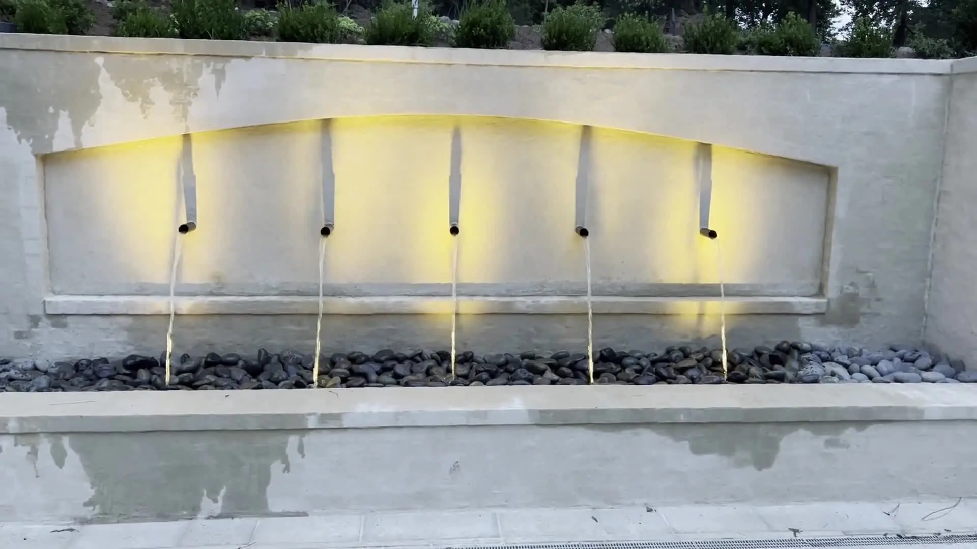 A plastered wall fountain with four lit scuppers pouring into a stone basin