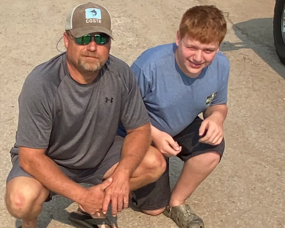 A man and a boy kneeling together on a job site