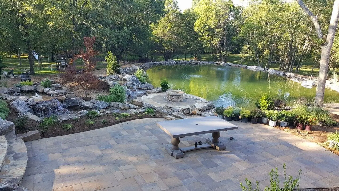 Paver patio with a stone table at the edge of a pond garden