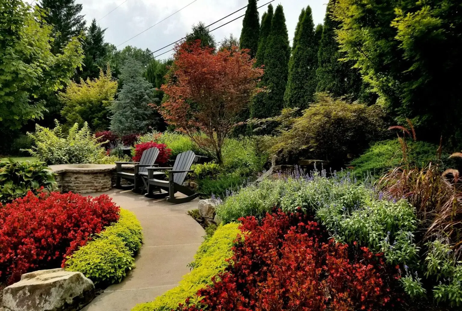 Red and gold flower beds along a curving garden path with two chairs