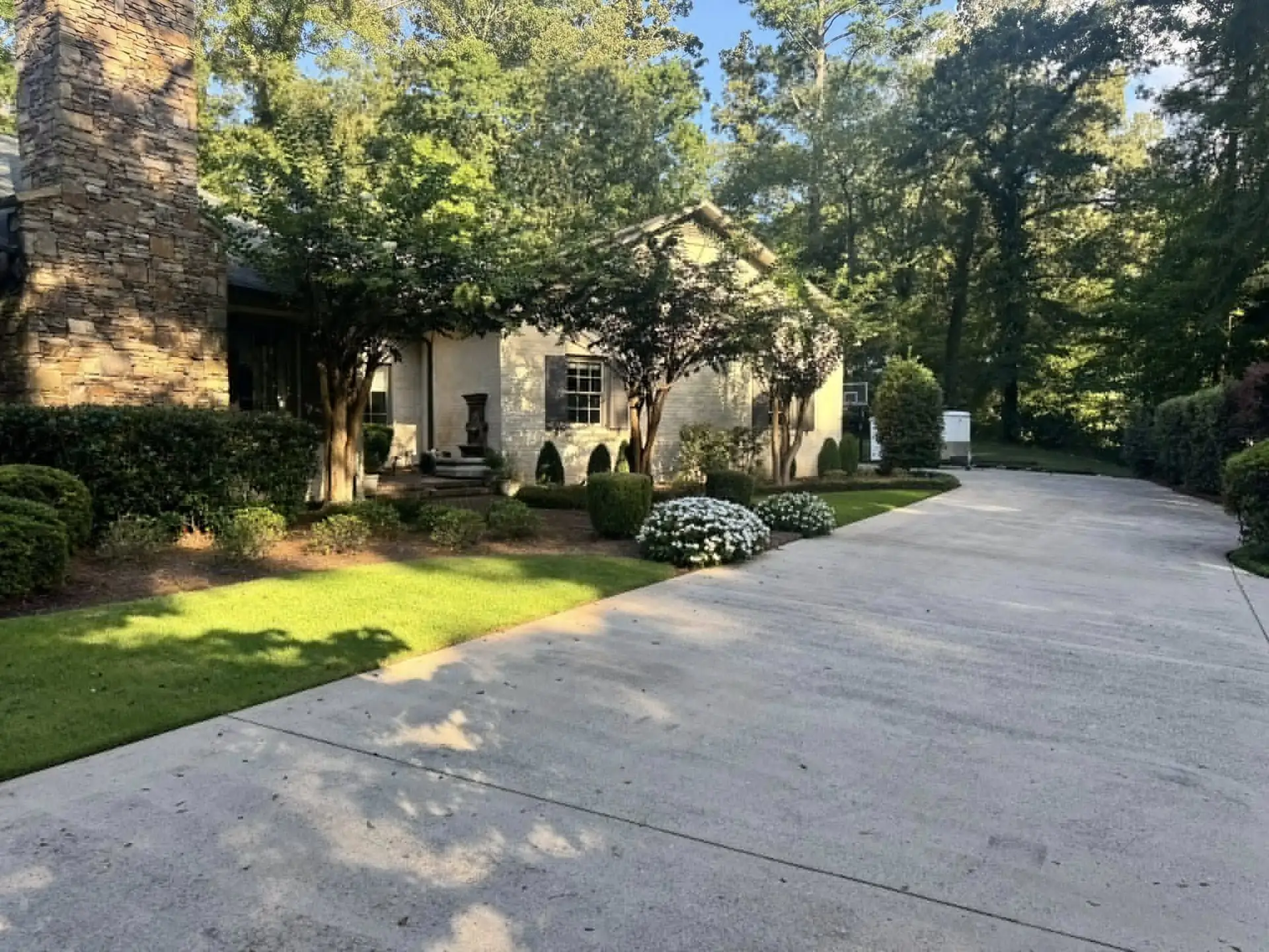 Shaded beds and lawn along the driveway of a stone house