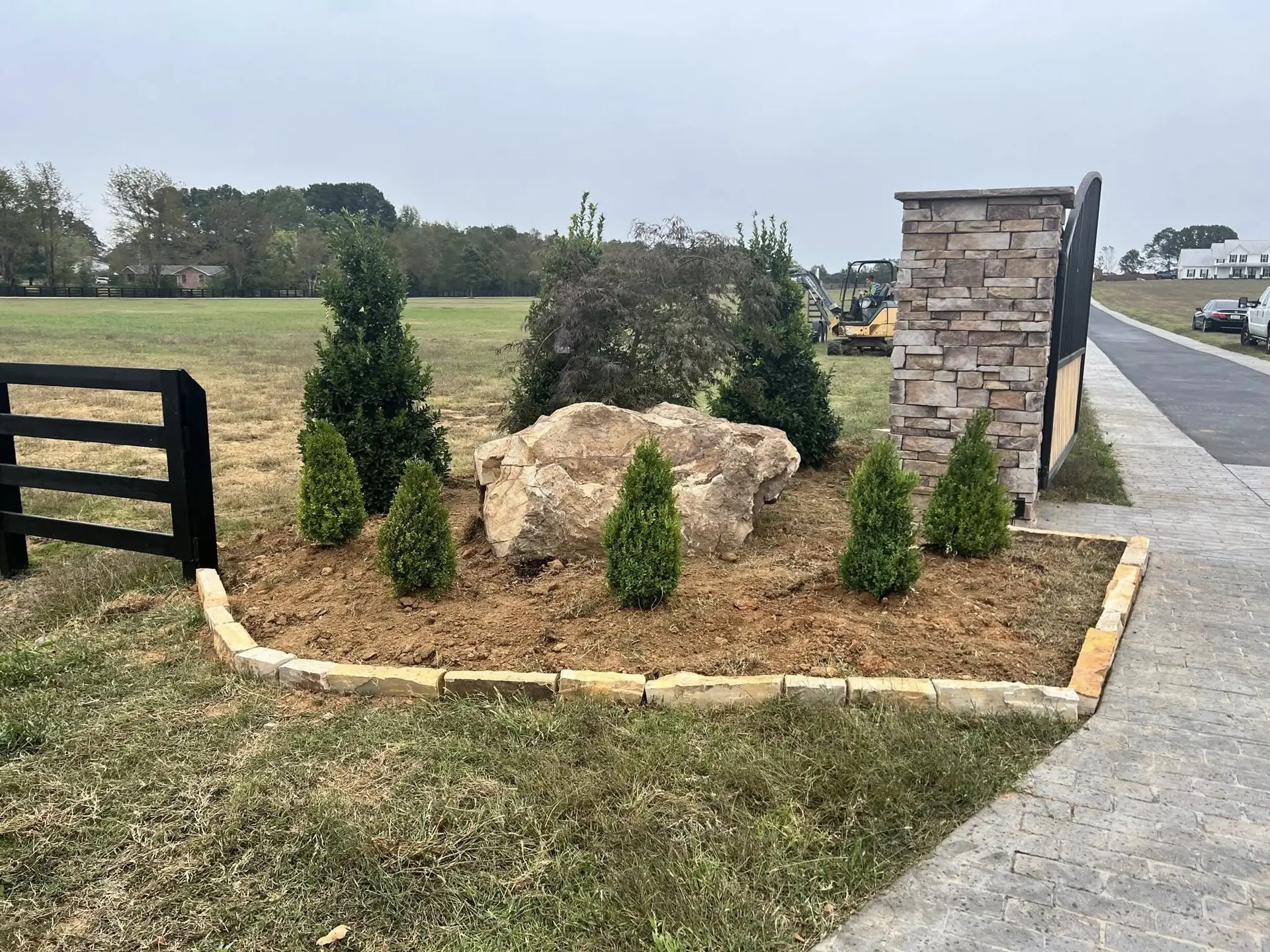 Stone entry pillars with a boulder bed of young evergreens