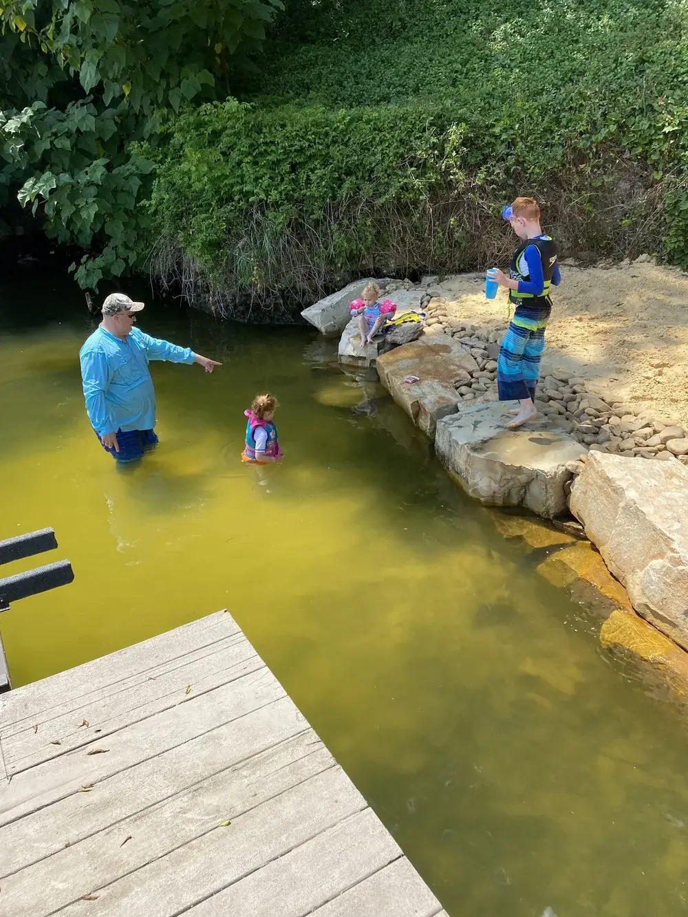 A family wading in a natural swim pond off a wooden dock