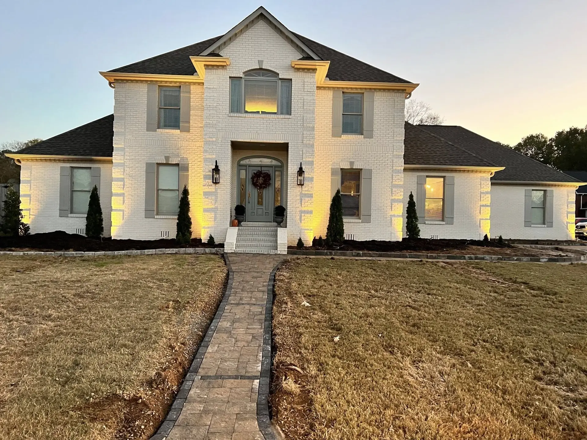 A white two-story house with its columns uplit at dusk